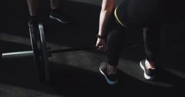 Kız gücü konsepti. Sinematik yakın çekim, genç bayan haç formundaki sporcu modern spor salonunda erkek koçla ağır halterleri kaldırıyor.