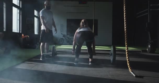 Женская тяжелая атлетика. Задний вид молодая спортсменка кросс-фитнес тренируется с тренером мужского пола, поднимающим штангу в современном спортзале. — стоковое видео
