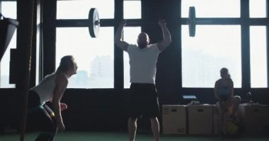 Genç erkek çapraz atletin sinematik çekimi ağır halterleri kaldırıyor, güzel bayan koç modern spor salonunda onu destekliyor..