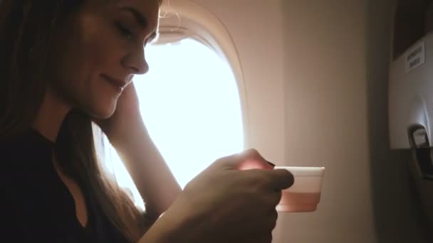 Młoda, szczęśliwa, zrelaksowana bizneswoman ciesząca się gorącym napojem, korzystająca z aplikacji smartphone messenger na siedzeniu okna samolotu. — Wideo stockowe