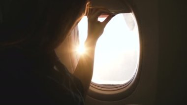 Mutlu kadın yolcunun uçak penceresini açtığı yakın çekim, sıcak içkinin ve uçuş sırasında muhteşem güneşli manzaranın keyfini çıkarırken.