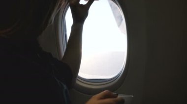 Mutlu yolcu kadının uçak penceresini açarken, içki içerken ve uçuş sırasında güzel gün ışığı manzarası seyrederken yakın çekim..
