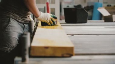 Yakından bir adam fabrikada büyük bir fırçayla ahşap kalas boyuyor. Erkek marangoz girişimci vernik tabakası üzerinde çalışıyor..