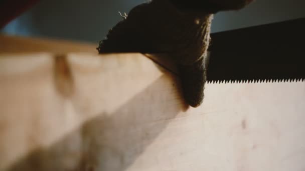 Filmové detailní mužské ruce v rukavicích řezání dřevěných prken úhly s ruční pilou na řemeslné dílně zpomalený pohyb. — Stock video