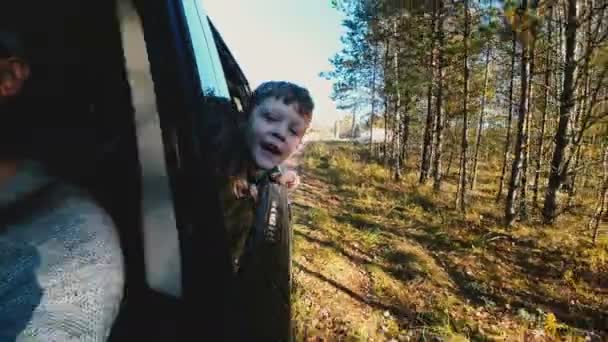 Feliz niño caucásico sonriente mirando por la ventana abierta del coche de conducción en el viaje familiar de verano en cámara lenta. — Vídeos de Stock