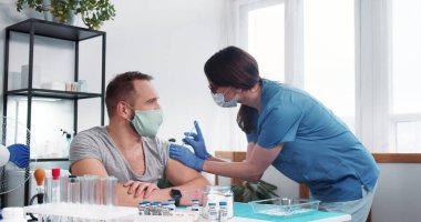 Aşı süreci. Mavi önlüklü genç hemşire kadın klinikteki erkek hastaya aşı aşısı yapıyor..