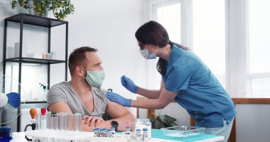 Aşı süreci. Mavi önlüklü genç hemşire kadın klinikteki erkek hastaya aşı aşısı yapıyor..