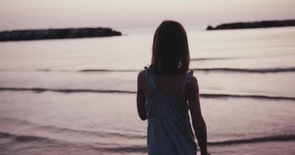 Silueta cu vedere din spate a unei adolescente care se plimba pe plaja calma apa de mare, bucurandu-se de rasaritul verii in vacanta slow motion . — Videoclip de stoc