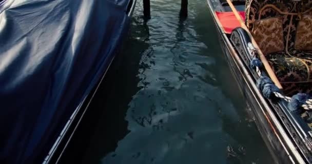 Slow tilt up on beautiful traditional gondolas parked at pier with no people, ancient buildings above channel in Venice. — Stock Video