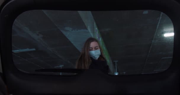 Vista interior del coche, joven mujer rubia de 30 años en la máscara de la cara abre la bota, pone bolsas de compras dentro en el estacionamiento, cierra la puerta. — Vídeo de stock