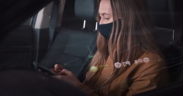 Крупним планом молода серйозна красива бізнес-леді в масці, використовуючи смартфон для роботи на автокріслі на парковці . — стокове відео