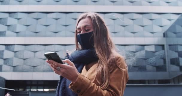 网上购物安全。在现代建筑中，年轻迷人的女商人戴着黑脸面具，使用智能手机移动应用. — 图库视频影像