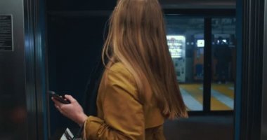 Pandemik tecritten sonra alışveriş. Mutlu, maske takan genç bir kadın asansöre akıllı telefon ve kese kağıdıyla giriyor..