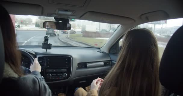 Widok z wnętrza samochodu, dwie biznesmenki w maskach rozmawiają podczas jazdy, skręcając w prawo wzdłuż ruchliwych ulic miasta. — Wideo stockowe