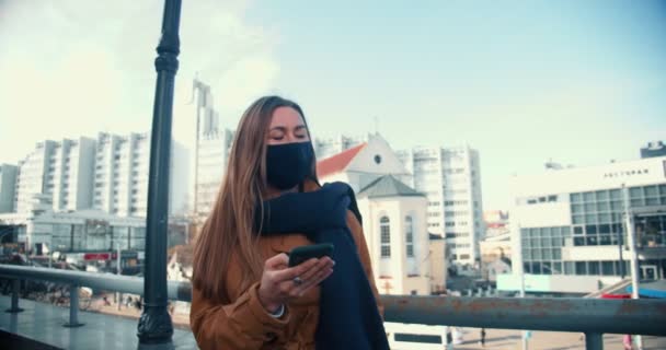 Conexión a Internet 5G. Joven atractiva mujer de negocios serena en la máscara facial utilizando el teléfono inteligente en el fondo de la ciudad de Minsk. — Vídeo de stock