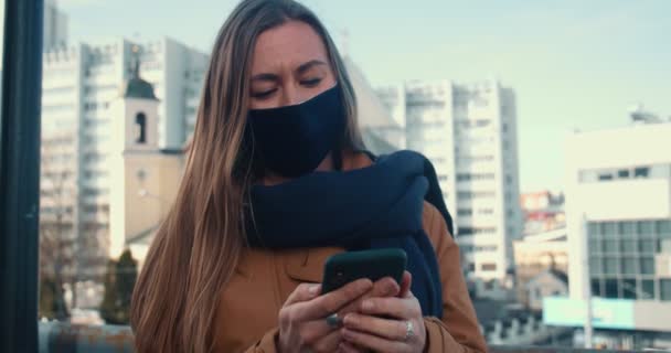 Porträtt av ung vacker affärskvinna i ansiktsmask med hjälp av smarttelefon mobilapp på solig Minsk stad bakgrund. — Stockvideo