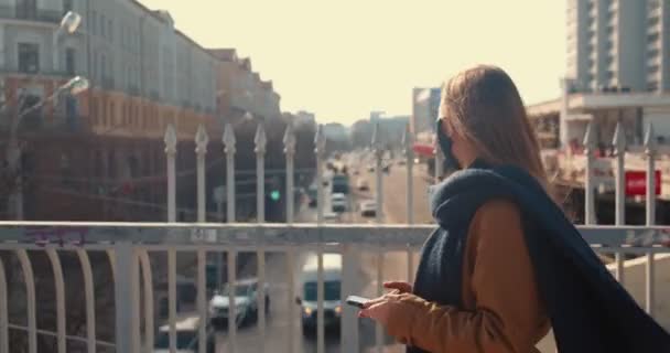 도시의 다리 주변을 걷고 있는 스마트 폰을 사용하여 얼굴에 마스크를 쓴 젊은 행복 한 사업가의 모습. — 비디오