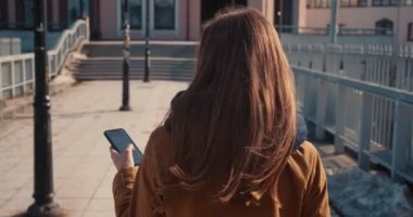 Yavaş çekim kamerası, güzel sarışın iş kadınını takip ediyor. Güneşli şehir köprüsünde akıllı telefon uygulaması kullanarak yürüyor..