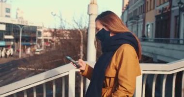 Sunny City Köprüsü 'nün arka planında yürüyen akıllı telefon uygulaması kullanan yüzü maskeli mutlu ve çekici bir kadın..