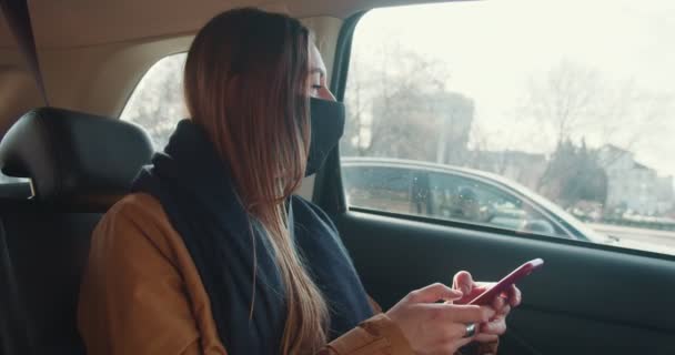 Koncept sociálních médií. Mladý krásný taxi cestující žena pomocí mobilní telefon app v autě zadní sedadlo nosí masku obličeje. — Stock video