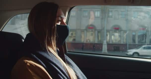 격리되어 있는 동안의 삶. 택시 뒷좌석에 앉아 얼굴 마스크를 쓴 채 창밖을 내다보는 아름답고 생각깊은 금발의 여성. — 비디오