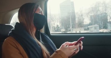 İlham konsepti. Genç, düşünceli taksi yolcusu arabanın arka koltuğundaki akıllı telefon uygulaması kullanarak yüz maskesi takan kadın..