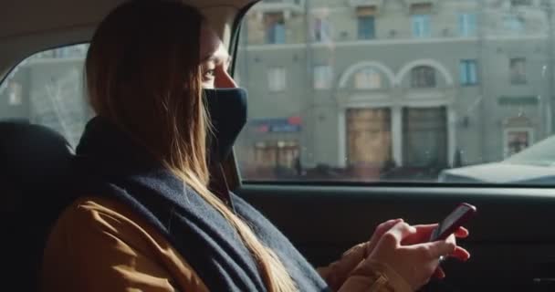 아름다운 젊은 승객 사업가가 스마트폰 앱 쇼핑을 이용하여 인터넷에서 얼굴 마스크를 착용 한 택시 뒷좌석 에서 — 비디오