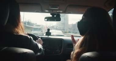 Trafiğe takıldım. Kalabalık şehir caddelerinde trafikte araba sürerken maskeli iki mutlu kadın konuşuyor..