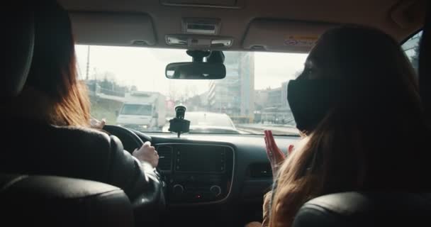 Κολλημένος στην κίνηση. Πίσω όψη δύο ευτυχισμένες γυναίκες με μάσκες προσώπου μιλούν κατά την οδήγηση σε βαριά κυκλοφορία κατά μήκος πολυσύχναστους δρόμους της πόλης. — Αρχείο Βίντεο