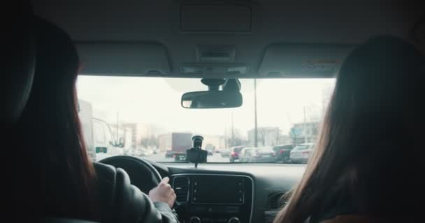 Widok z tylnego siedzenia, dwie piękne szczęśliwe przyjaciółki w maskach twarzy rozmawiać podczas jazdy samochodem wzdłuż ruchliwych ulic miasta. — Wideo stockowe