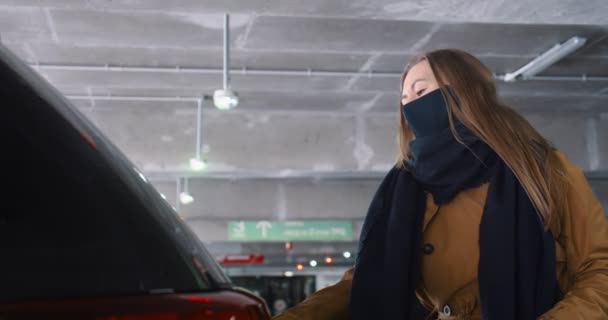 Nakupovat po karanténě. Šťastná mladá žena v masce otvírá kufr auta, dává nákupní tašky na parkovišti obchoďáku. — Stock video