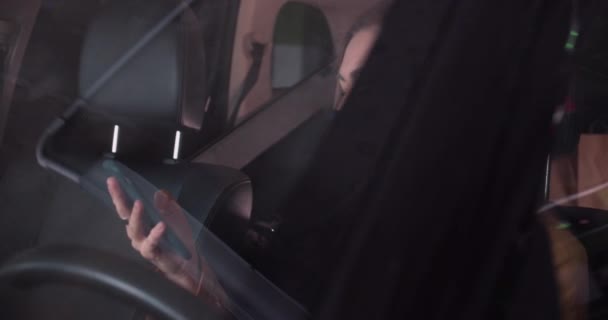 Cinematic shot, jonge dertiger jaren mooie blonde vrouw in het gezicht masker met behulp van smartphone om nieuws te lezen zitten in de auto bestuurder stoel. — Stockvideo