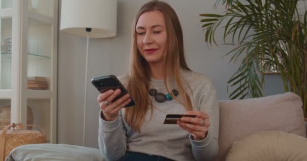 Linda feliz animado jovem blogueiro mulher entra detalhes do cartão de crédito no aplicativo de pagamento smartphone compras de casa. — Vídeo de Stock