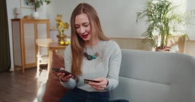 İnternetten alışveriş konsepti. Güzel, heyecanlı sarışın kadın kredi kartı ve akıllı telefon ödeme uygulaması kullanarak başarıyı kutluyor.
