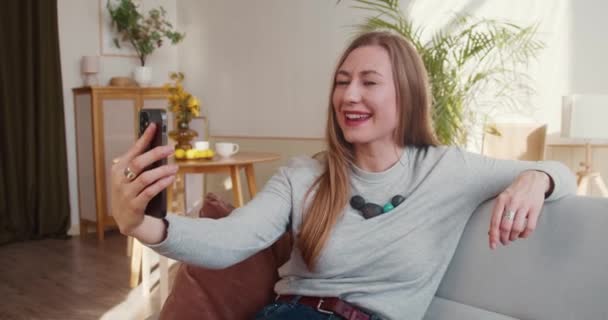Додаток для веб-конференцій. Щаслива приваблива молода блондинка посміхається, використовуючи смартфон відеодзвінок, щоб поговорити з друзями онлайн . — стокове відео