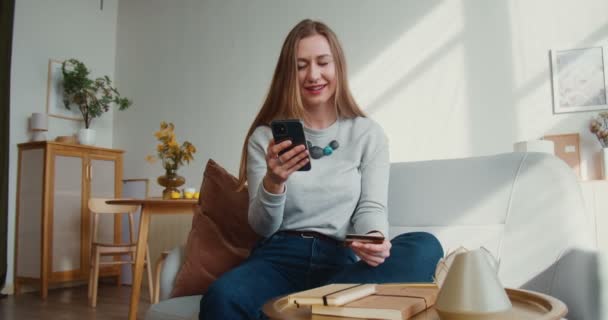 Betalningssäkerhet online. Ung glad säker blond kvinna skriver in kreditkortsuppgifter i smartphone shopping app hemma. — Stockvideo