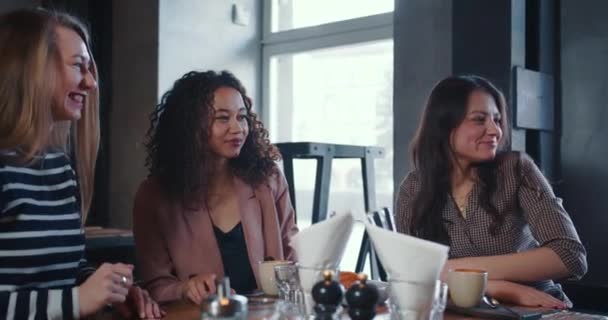 Tre giovani felici attraenti amici femminili multietnici sorridenti si incontrano al caffè alla moda per pranzo, servito cibo dalla cameriera. — Video Stock