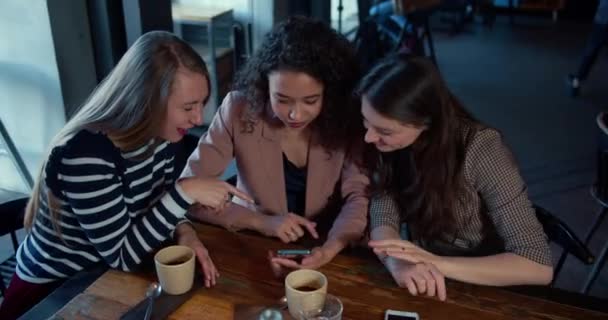 Hoge hoek drie jonge mooie gelukkig multi-etnische vrouwelijke vrienden gebruiken smartphone e-commerce app zittend aan cafe tafel. — Stockvideo