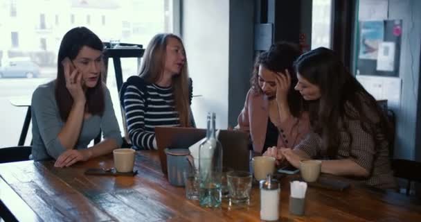สี่คนมีความสุขตื่นเต้นสาวสวยเพื่อนผู้หญิงที่หลากหลายนั่งและพูดคุยอย่างสบาย ๆ ที่การประชุมโต๊ะร้านกาแฟสมัยใหม่ . — วีดีโอสต็อก