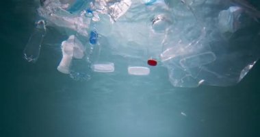 Plastik atık okyanusu kirletiyor. Su altında, çöp ambalajının sinematik görüntüsü ışık ışınları altında ağır çekimde yüzüyor..