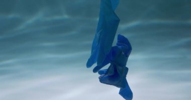 Kirlenmiş okyanusta salgının sonuçları. Atılmış tek kullanımlık mavi tıbbi eldivenler suyun altında ağır çekimde yüzer..