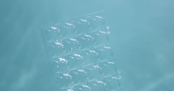 水中プラスチック廃棄物汚染。近くに捨てられた卵ホルダートレイが薄緑色の海の背景に浮かぶスローモーション — ストック動画