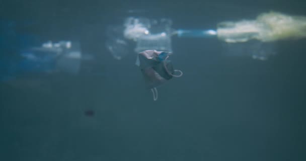Крупним планом медична маска для обличчя плаває під водою з різними пластиковими сміттями на поверхні океану повільний рух . — стокове відео