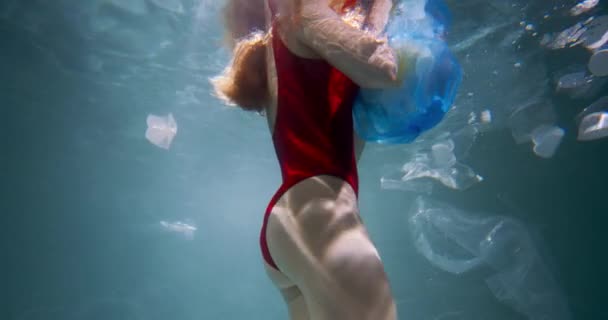 プラスチック汚染の概念。若い観光客の女性は、水の遅い動きの下で単一の使用廃棄物と青いゴミ袋を保持. — ストック動画