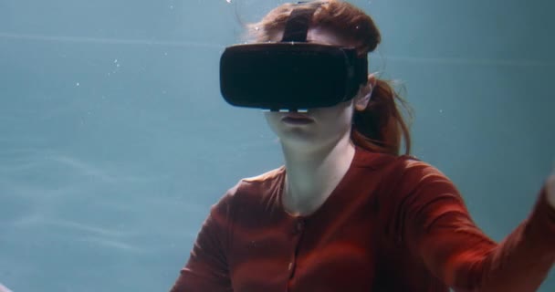 Окунулся в виртуальную реальность. Молодая красивая улыбающаяся рыжая женщина с помощью VR гарнитуры плавает под водой замедленным движением. — стоковое видео