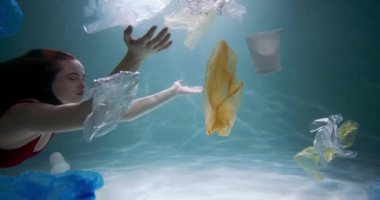 Güzel bir dişi turist tek kullanımlık ambalaj yoluyla suyun altında yüzer. Plastik atık kirliliği sorunu yavaş çekim.