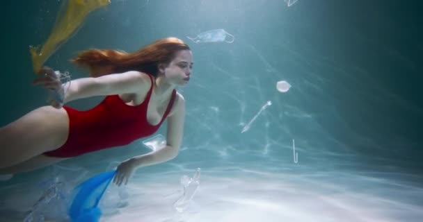 Jeune belle nage touristique féminine à travers des sacs à usage unique. Pollution plastique non recyclable sous l'eau au ralenti. — Video