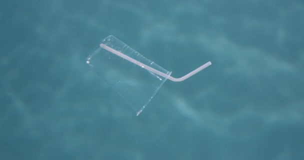 Underwater plastic. Close-up discarded single use cup with straw floating under water in blue sea background slow motion — Stock Video