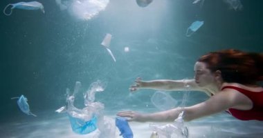 Suyun altında sinematik, genç ve güzel bir bayan turist plastik atıkların arasında yavaş çekimde yüzüyor..