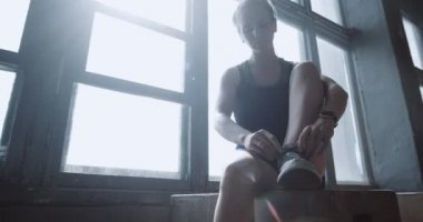 Spor ayakkabısı bağcıkları bağlayan genç, güzel sarışın kadın spor salonunda ağır çekimde egzersiz yaptıktan sonra dinleniyor..